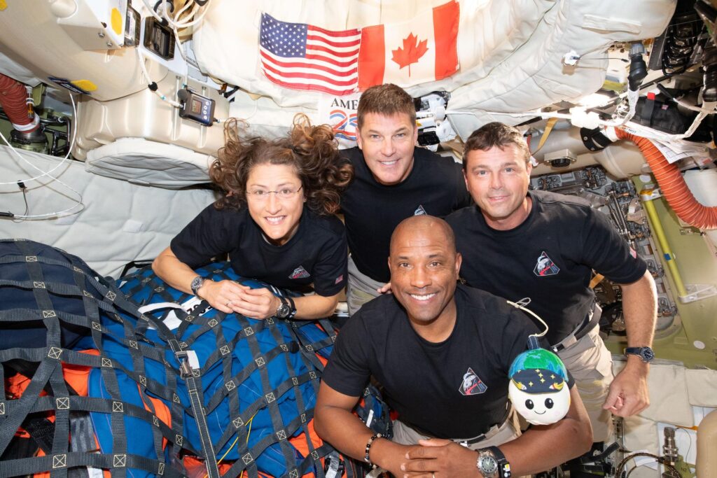 Artemis II crew group photo with their zero gravity indicator "Rise" inside the Orion spacecraft on their way home
