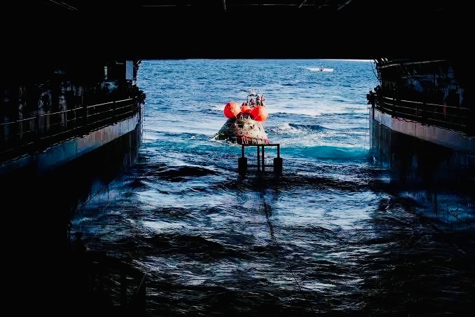 Orion spacecraft being guided into flooded well deck of recovery ship